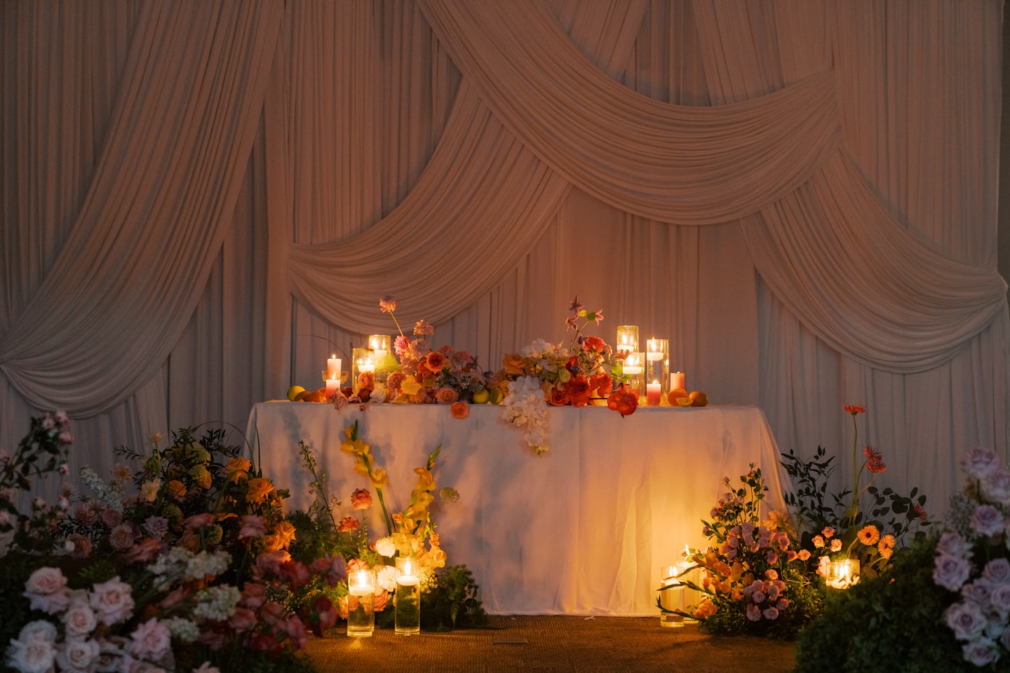 Wedding table decorated with orange floral arrangements and lit candles.